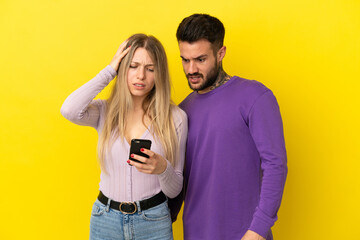 Young couple over isolated yellow background reading a message with the mobile