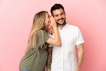 Pregnant woman and man over isolated pink background whispering something