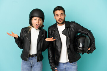 Couple with motorcycle helmet over isolated blue background with surprise and shocked facial expression