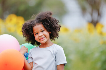 childhood and back emotion concept- little african american curly hair girl playing bolloons near sunflower field at outdoor.