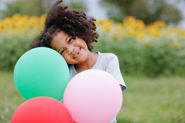 childhood and back emotion concept- little african american curly hair girl playing bolloons near sunflower field at outdoor.