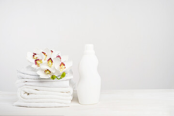 Stack of white linen, washing gel and fabric softener on a white table with orchid flowers. Mockup...