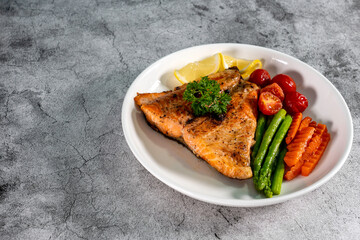Salmon steak with vegetables, asparagus, carrots, green peas, lemon, pepper on cement background.