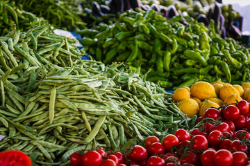 Close-up of beautiful rows of fresh vegetables in a market showcase: green peas, peppers, lemon, cherry tomatoes.