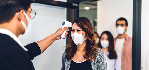 Group of professional asian business and using infrared thermometer for checking body temperature staff fever before work in quarantine for coronavirus wearing protective mask at office - obrazy, fototapety, plakaty