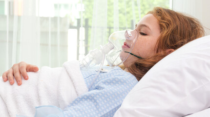Cute little asian girl with oxygen pipe and using oxygen mask for inhalations and treatment on her face on bed in the hospital.health care,support concept