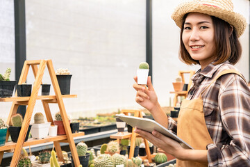 Asian farmer learning and check young Echinopsis cactus in hands gently with tablet on house background. Decorative plants can be used to decorate the living room and living room or on the desk.