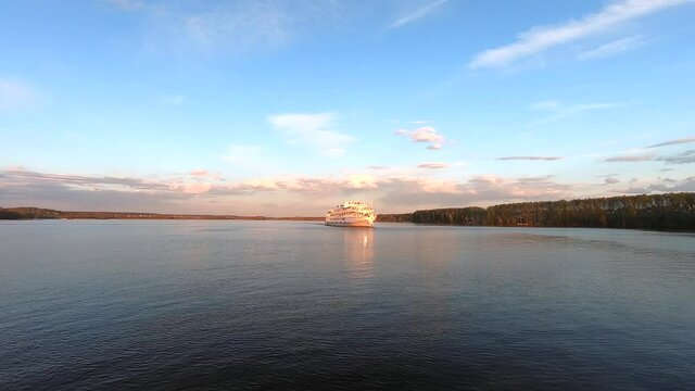The passage of a large passenger ship along the river at sunset. Beautiful colorful landscape of the river against the background of the blue sky at sunset. Traveling by ship on the river