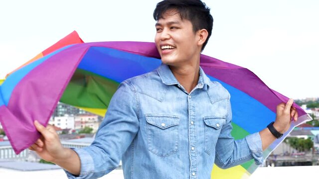 slow motion scene on asian young gay man hold and raise waving lgbt flag to celebrate and cheer with proud feeling for pride month festival concept