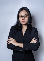 Portrait of serious thoughtful businesswoman in black confident suit, isolated over gray background. Pretty girl wearing glasses and black suit standing with crossed arms. Business studio concept.