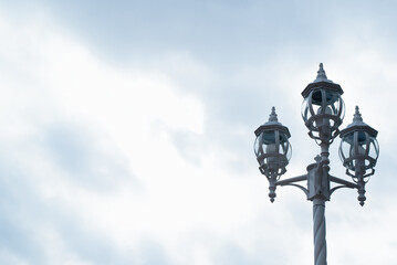 Fototapeta na wymiar Vintage lantern on the street, against the backdrop of a cloudy sky. Three lamps on a decorative pole. Copy space