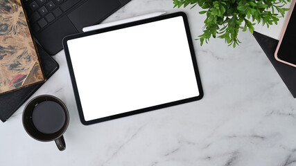 Modern workspace with digital tablet, coffee cup, houseplant and notebook on marble table.