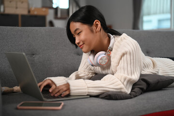 Young asian girl tying on sofa and using laptop computer.