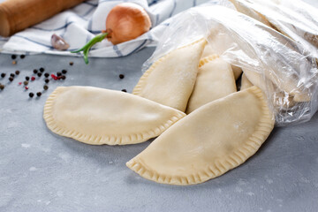 Frozen chebureks in the bag on grey table with ingredients. Traditional food.