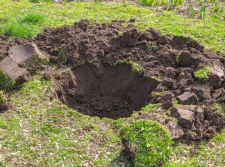 Planting hole and a soil heap on the lawn prepared for a tree planting, environment and ecology concept