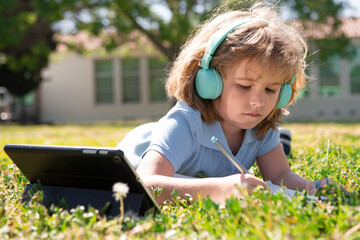 Child homework outside in scholl yard. Little schoolboy pupil with tablet in the park on grass....