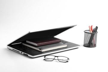 Modern workspace with laptop keyboard, notebook, spectacles on white background.