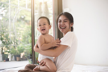 Obraz na płótnie Canvas Asian mom and baby smiling happiness in living room together. Female stay at home with her son. Mom and baby in mother’s day concept.