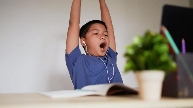 slow motion scene on asian kid boy stretching body and yawning while studying online on school e-learning webinar program in house for homeschool technology lifestyle concept