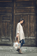 A young pretty brunette dressed in a light beige wide cardigan and blue ripped jeans wears a beautiful original boho bag and short ankle boots. Leather Boho Crossbody Bag, Hobo Boho Shoulder Bag.