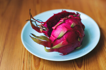 Red Dragon Fruit, tropical fruits in Indonesia Southeast Asia. Cut into half in blue round ceramic plate on top of wood background. It may help lower your blood sugar.