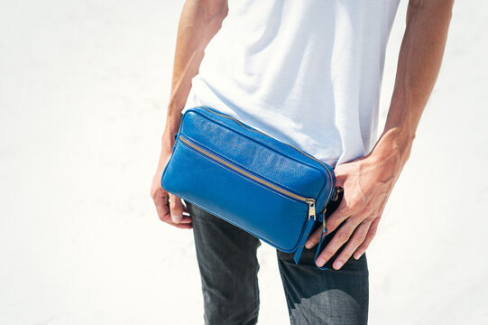 Leather Convertible Blue Belt Bag Men. The guy stands on a white background, wears a white T-shirt, black jeans and a fashionable belt bag.