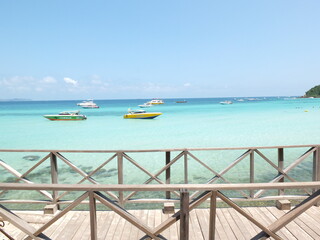 The wooden bridge by the sea has boats and clear sea and sky.