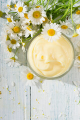 chamomile flowers and baby cream on white wooden table, directly above