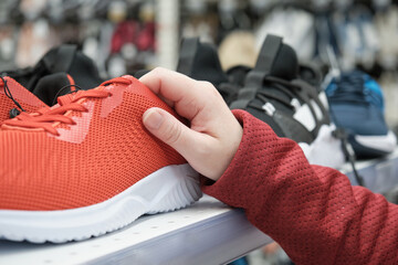 Woman in a shoe store chooses to buy, red sports sneakers in a mesh for walking and running. The concept of sports and shopping. Hands close up shot