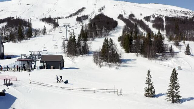 Ski mountain slope piste over view shot. Drone rising over skiing area on sunny day in winter. Downhill tracks and cross-country skiing with kids in pulk or sled baby in tow