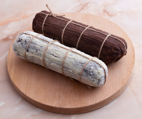 Brown and white salami made by chocolate and biscuits on a wooden round plate