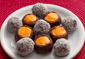 Balls of chocolate and biscuits, cookies of cocoa and orange cream on white plate and red background