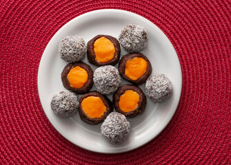 Balls of chocolate and biscuits, cookies of cocoa and orange cream on white plate and red background