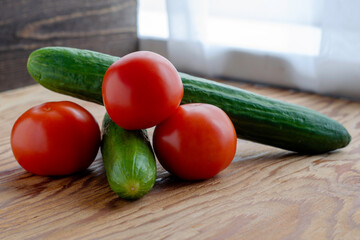 two cucumbers and three tomatoes on a wooden background