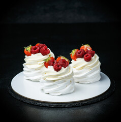 Pavlova pie with raspberries and strawberries on a black background. Meringue with cream and berries. Space for text
