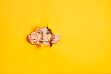 Cheerful happy face of child looking into hole in torn yellow paper wall. Sidebar for text, promotional information, advertising, positive news, events, sale, discount, best choice.