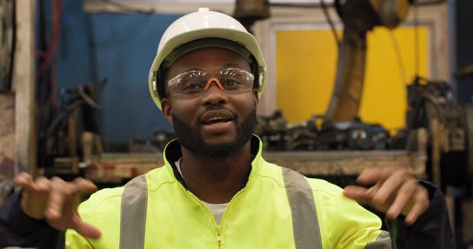 POV Portrait of professional industrial engineer African american man using video call to explain automation robot arms machine in manufacturing industry Factory. Technology and Innovation concept.