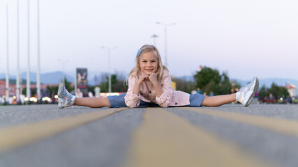 A smiling 7-year-old girl sits in a twine in a public square. Outdoor gymnastics.