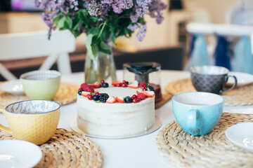 Happy Birthday at home, teatime. Birthday cake, cups, bouquet of lilacs on kitchen table