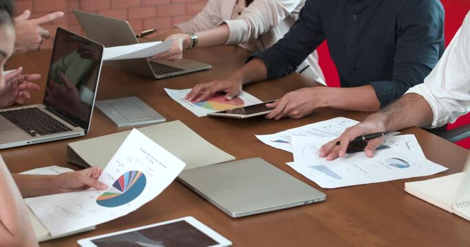 A group of young, hard-working Asian employees male and female discussing about company data in the papers, computer and digital tablet. The office workers thinking about solutions for business plan.