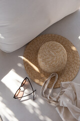 Flat lay of women's fashion accessories. Stylish female sunglasses, straw hat, shopper bag on white lounge couch with pillows. Creative composition for fashion blog, web, social media. Top view