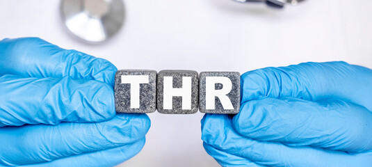 THR Total hip replacement - word from stone blocks with letters holding by a doctor's hands in medical protective gloves - obrazy, fototapety, plakaty
