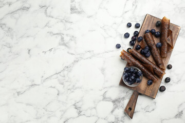 Delicious fruit leather rolls and blueberries on white marble table, flat lay. Space for text
