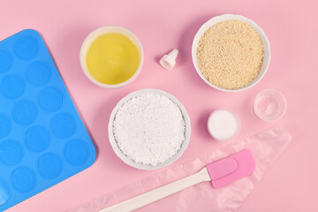 Ingredients for making homemade French Macarons sweets including powdered sugar, ground almonds, egg white, salt and baking tools on pink background