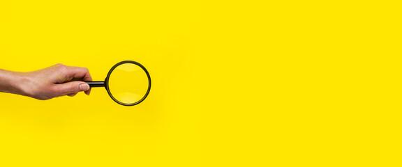 female hand holds a magnifying glass loupe on a yellow background. Banner