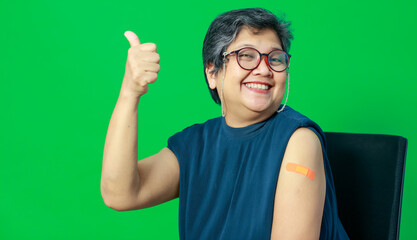 Fototapeta premium Smiling adult senior Asian woman smile with confident show shoulder with band aid plaster after getting Coronavirus of Covid-19 vaccine injection. Idea for vaccination of population against virus