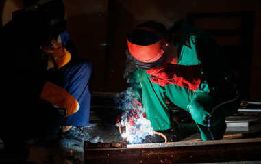 mechanics workers work overtime hardly at night in a factory. Engineers wearing safety outfits with mechanic jumpsuits, gloves, boots, and welding helmets working on metal welding