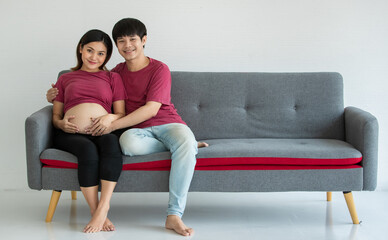 Fototapeta na wymiar young family husband and wife sitting on a couch. They are smiling and looking at a camera. A man and pregnant woman touching on a belly. Expecting a healthy baby