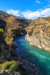 Fototapeta na wymiar The Kawarau River in the South Island of New Zealand, passing through a narrow gorge with autumn trees on top of the cliffs 