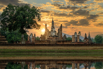 Naklejka premium Buddha statue and pagoda Wat Mahathat temple with reflection during dramatic sky sunset, Sukhothai Historical Park, Thailand
